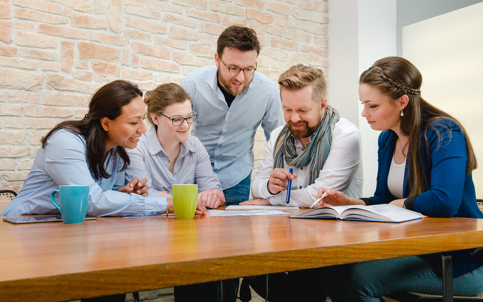 Image of five IVU employees sitting around a table and studying different documents