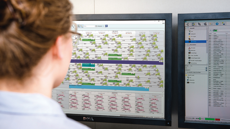 A woman sits in front of two monitors running the IVU.crew software and a QR code of a 3G certificate. A woman sits in front of two monitors running the IVU.crew software and a QR code of a 3G certificate.