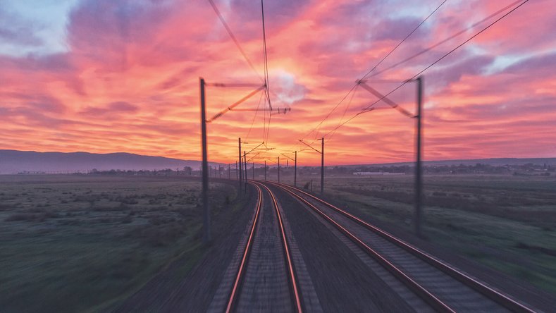 Zweigleisige Bahnstrecke bei Sonnenuntergang mit rotem und orangefarbenem Himmel