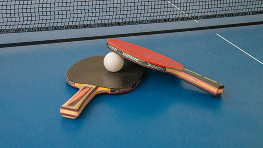 Two table tennis bats lie on top of each other on a table tennis table with a table tennis ball in between