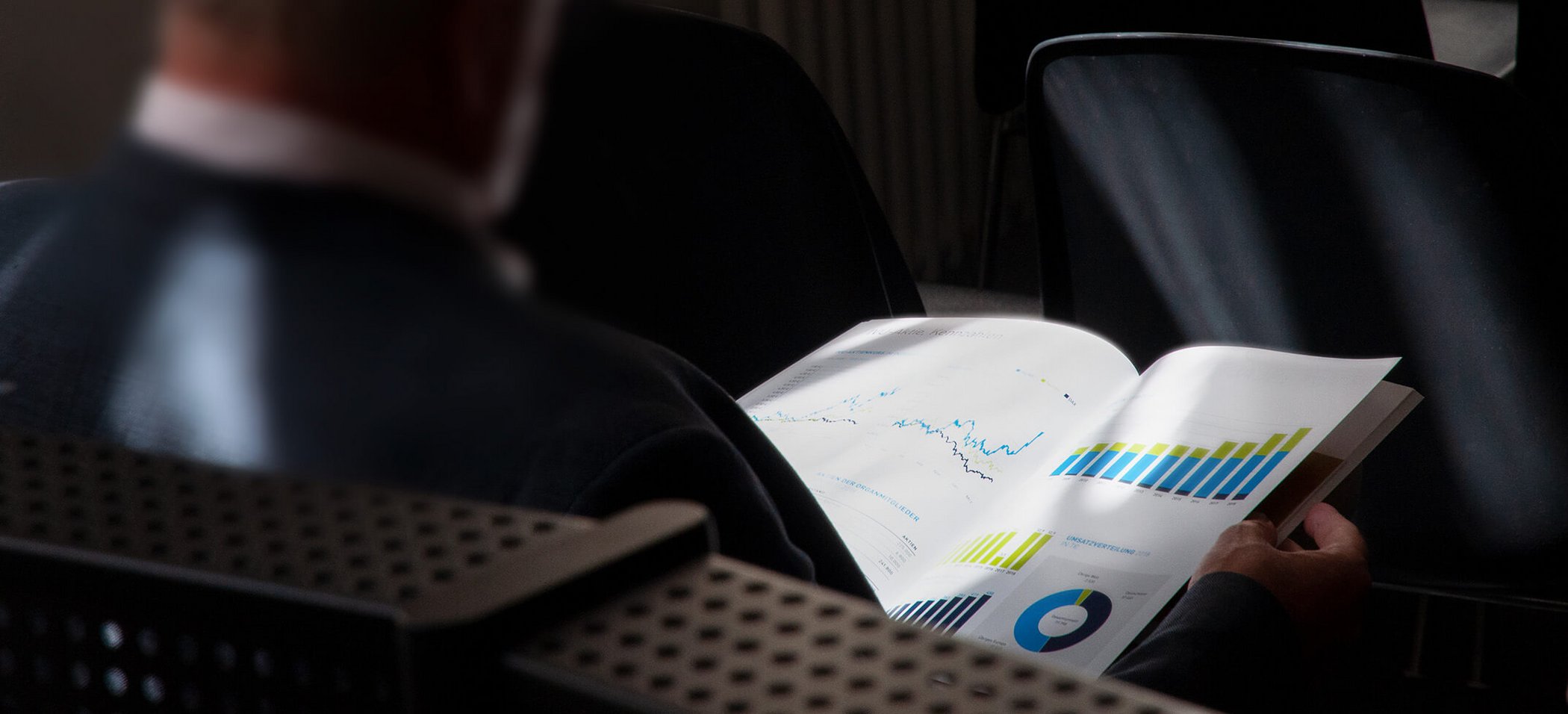 Sitting man from diagonally behind holding IVU annual report openly in his hand