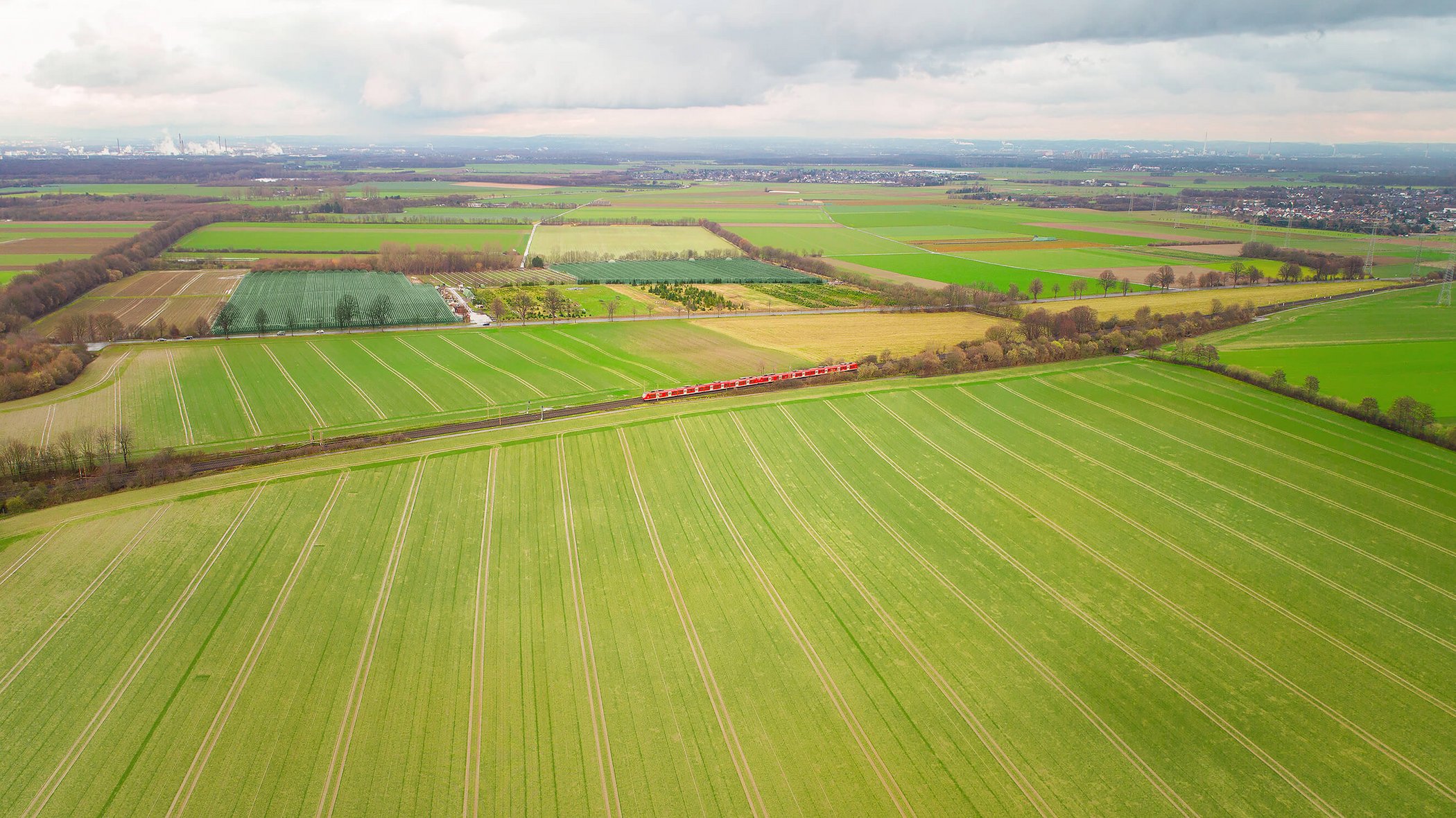 Aerial view of red regional train on railway line through green agricultural landscape