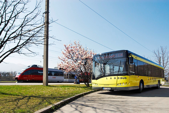Photo of a moving yellow bus next to a moving red and white train