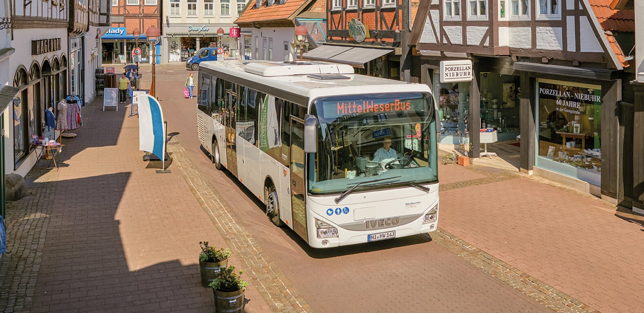 White city bus with destination display at bus stop in pedestrian zone with shops