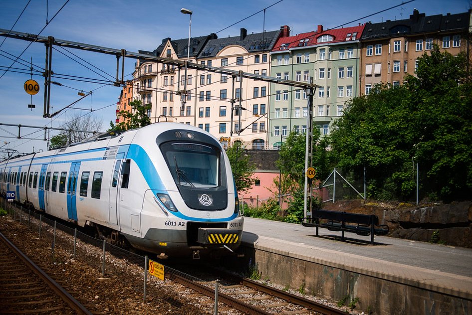 An MTR Pendeltågen train stops at a platform in Stockholm in front of a row of buildings