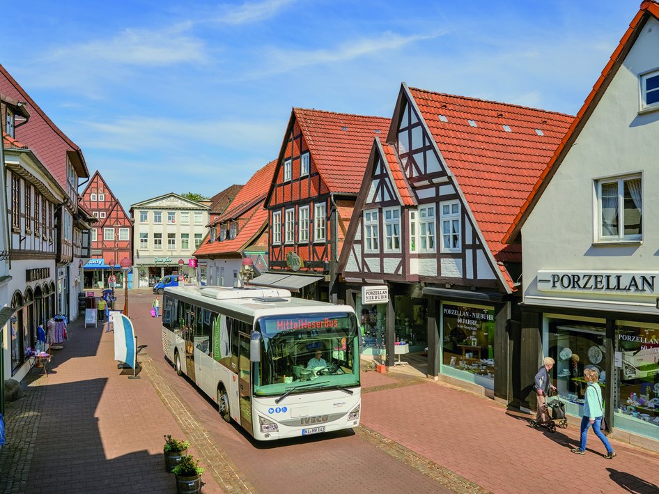 White city bus with destination display at bus stop in pedestrian zone with shops