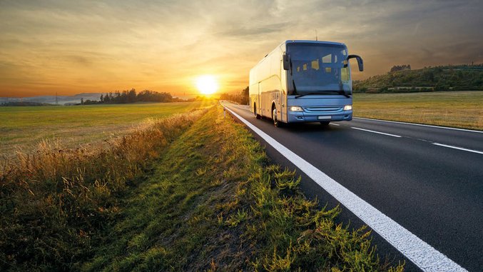 Weißer Fernbus auf Landstraße bei Sonnenuntergang mit weitem Feld