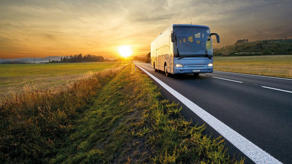 Weißer Fernbus auf Landstraße bei Sonnenuntergang mit weitem Feld