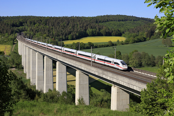 A white ICE train crosses a bridge in front of a green landscape