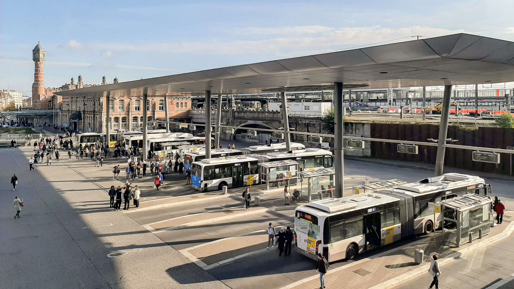 Multiple city buses and passengers at central bus station with covered platforms