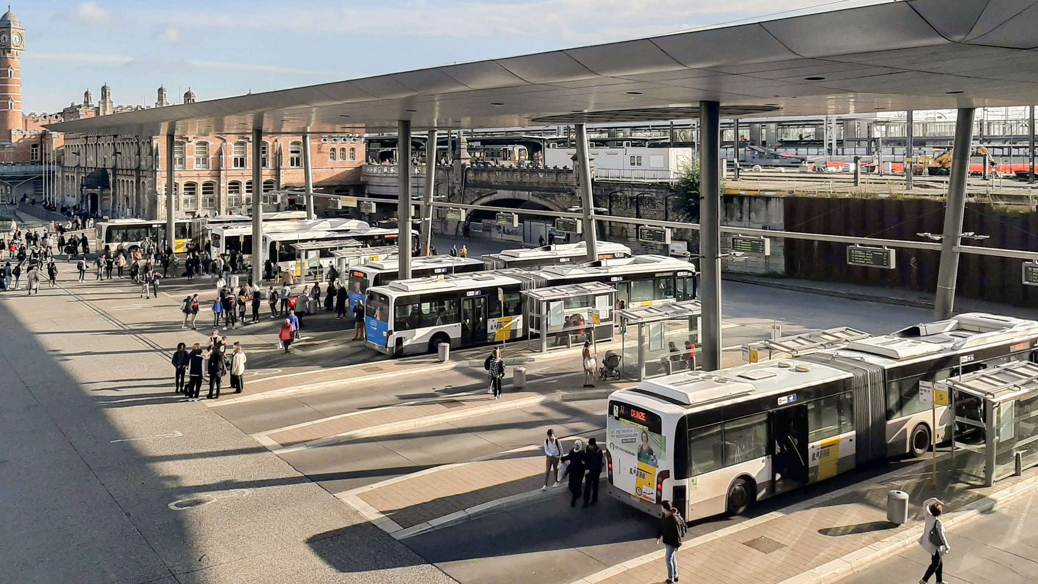 Multiple city buses and passengers at central bus station with covered platforms