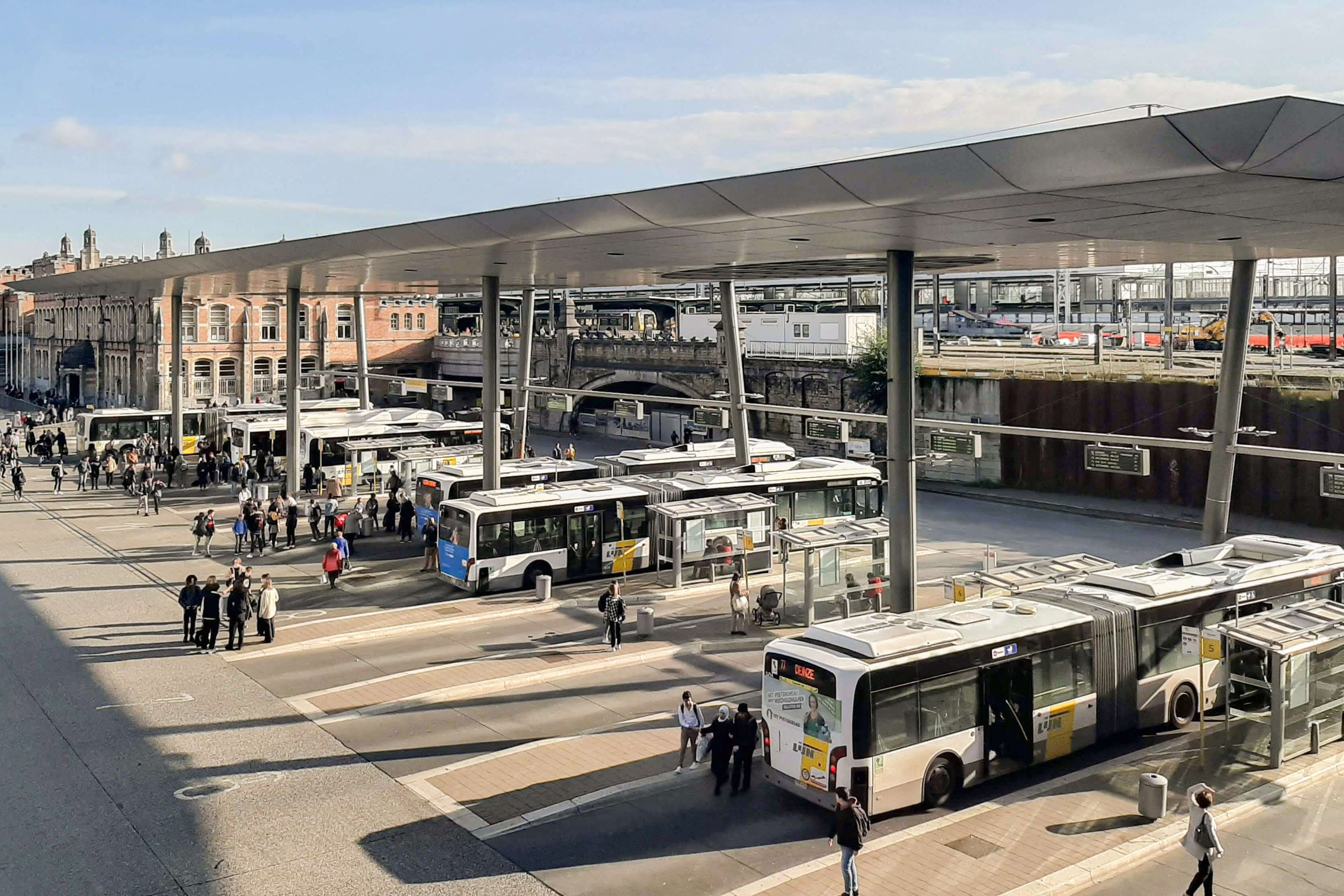 Mehrere Linienbusse und Fahrgäste an zentralem Busbahnhof mit Überdachung