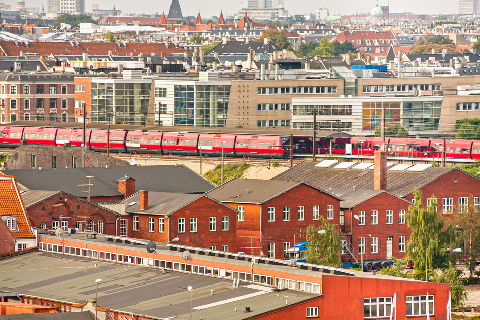 Aerial of two red DSB trains at a station between houses in Copenhagen.