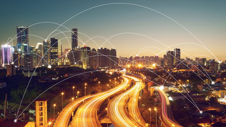 Skyline nocturne avec autoroutes illuminées et nœuds connectés symbolisant la mobilité numérique