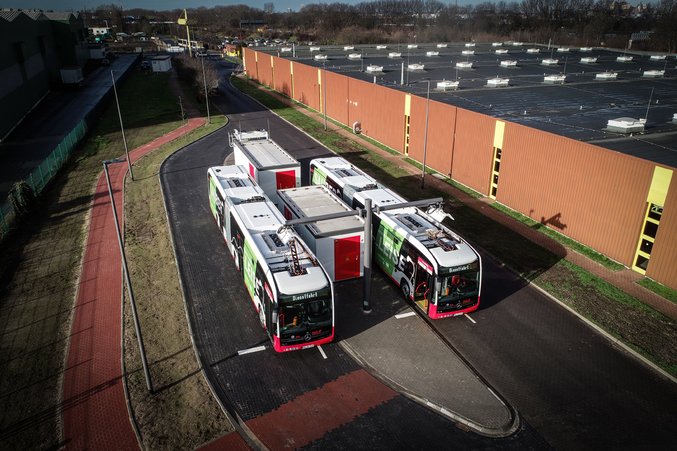 Bird's eye view of three white-red city buses at bus depot next to industrial building