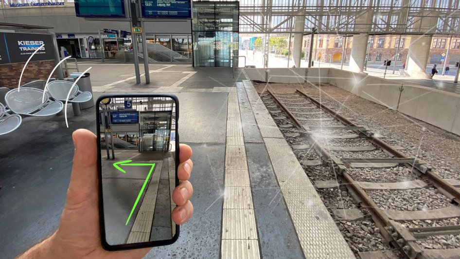 Hand hält Smartphone mit App-Anzeige auf leerem Bahnsteig mit Gleisen