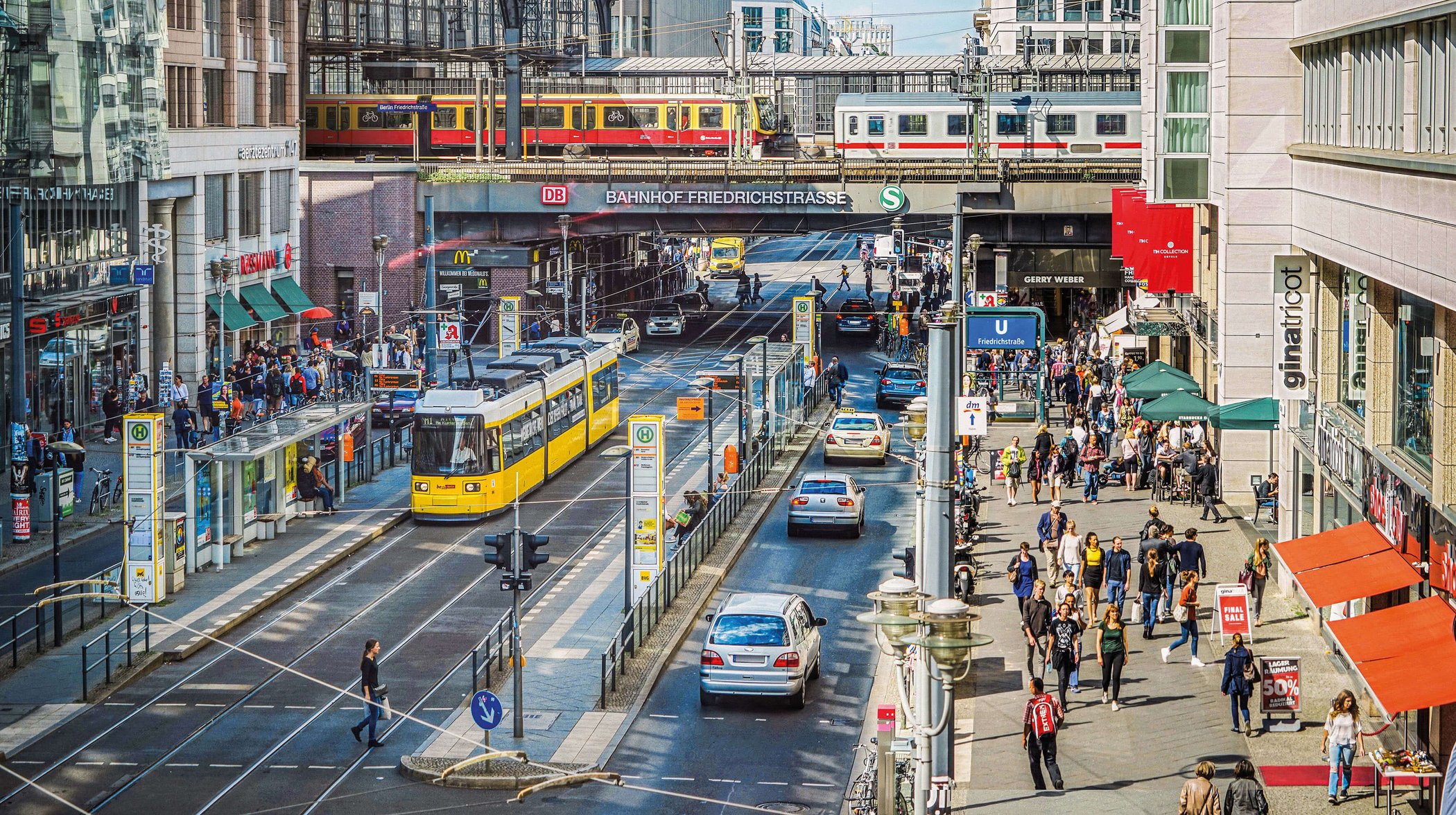 Busy Friedrichstraße in Berlin with S-Bahn, yellow tram, pedestrians and Friedrichstraße station in the background