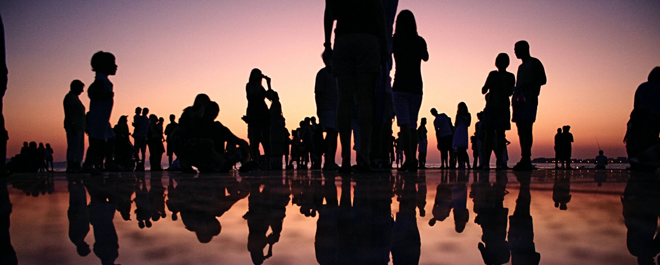 Black silhouettes of people by the water at sunset