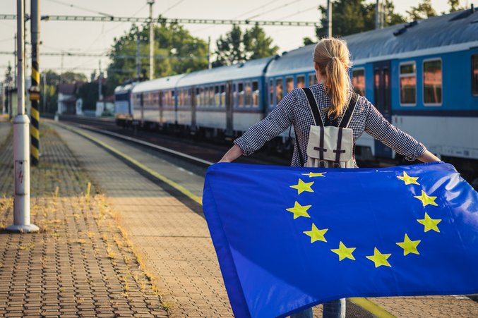 Person hält EU-Fahne an Bahnsteig mit blauem Zug im Hintergrund