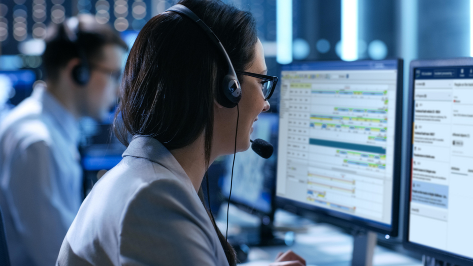 Two employees work at several monitors in a railway control centre.