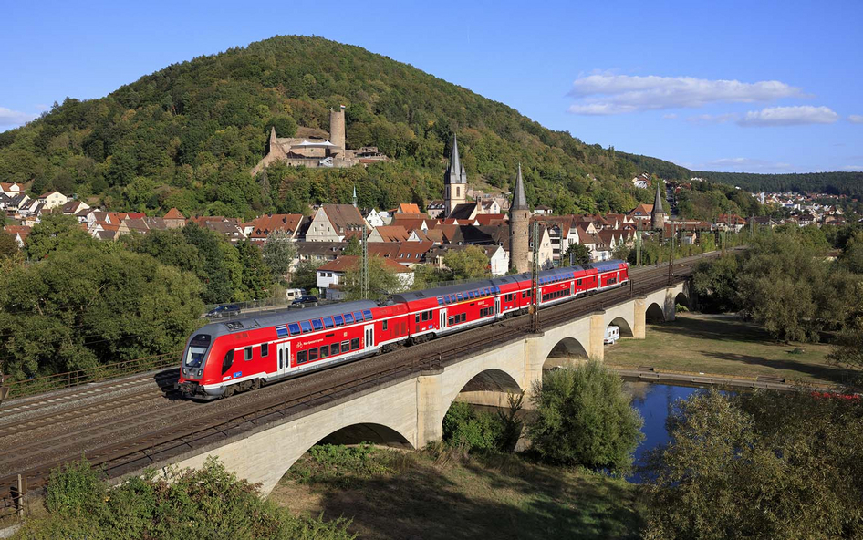 Red DB Regio Twindexx double-deck train crossing a bridge in front of a scenic landscape