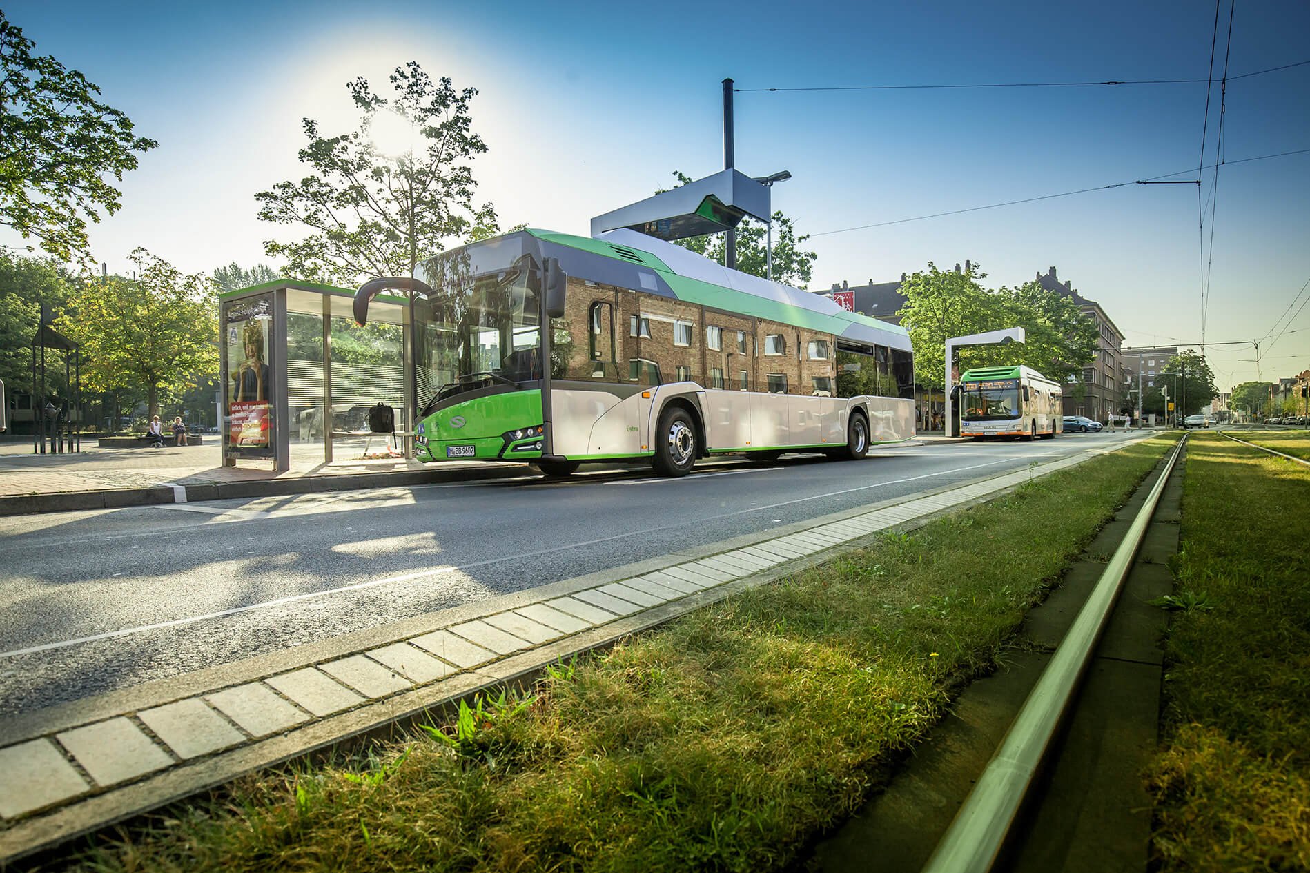 Green and white electric bus charging at station with solar roof in urban environment