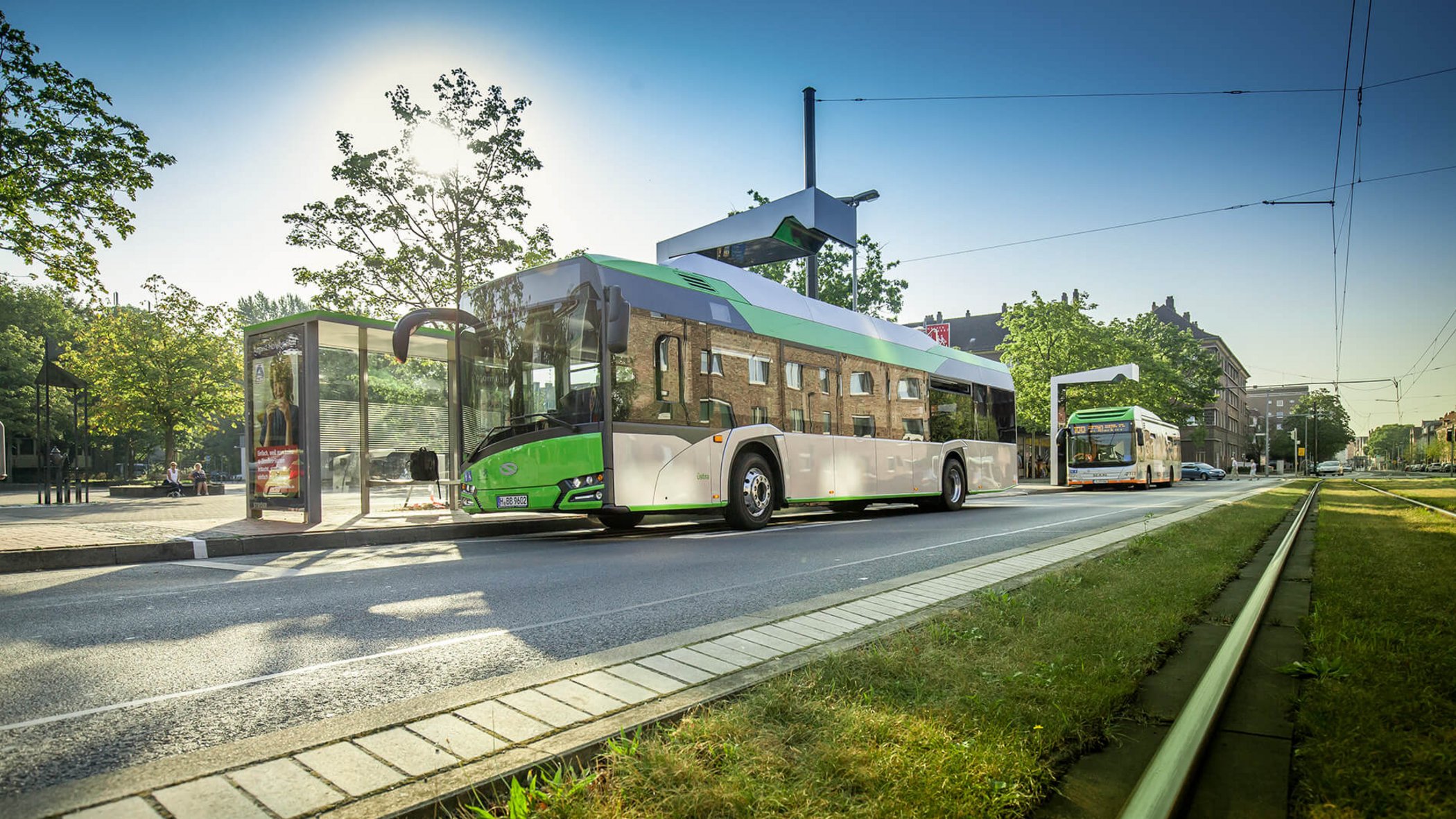 Bus électrique vert et blanc en charge à une station avec toit solaire en milieu urbain