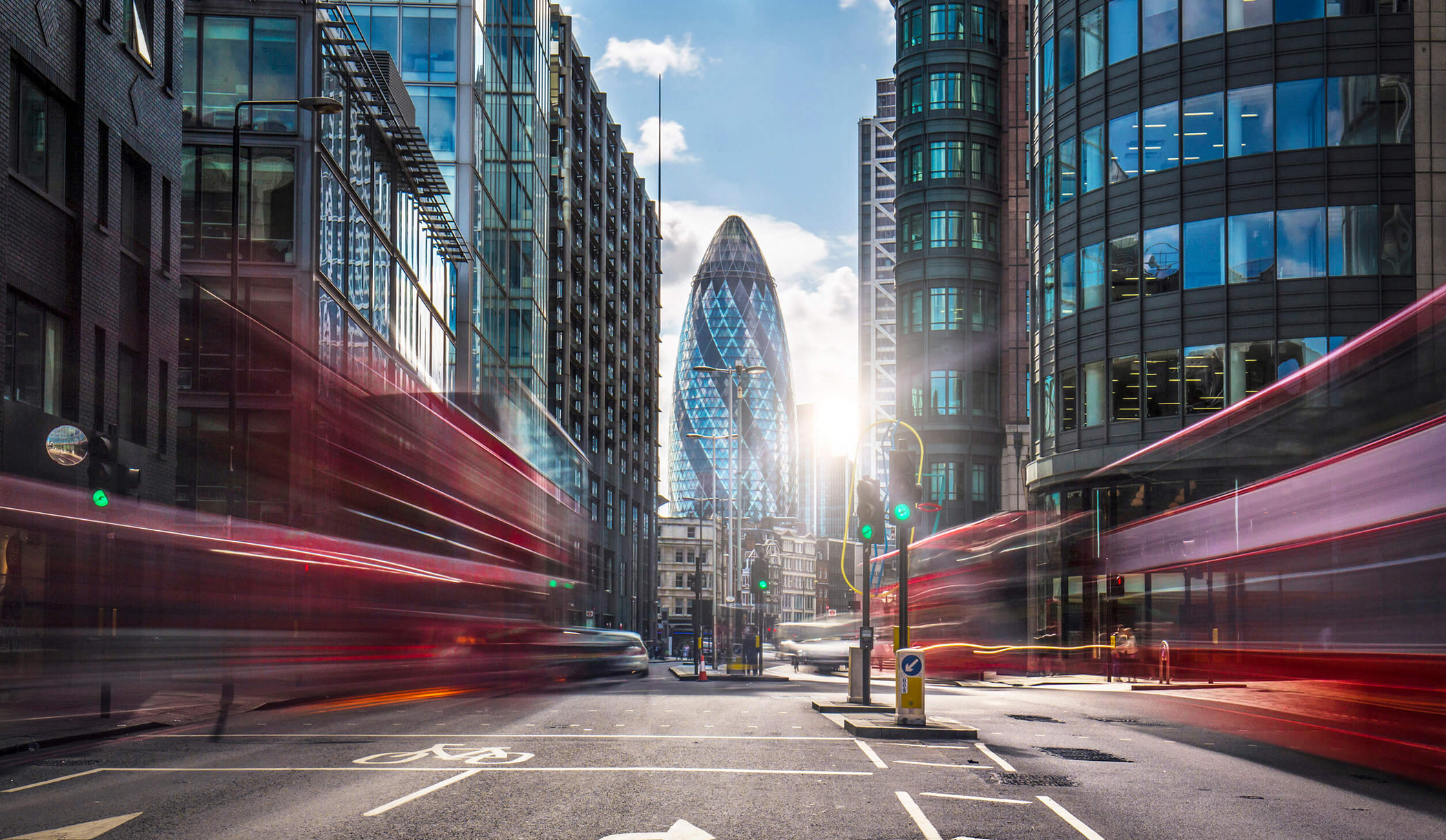 View of The Gherkin in London through two houses through buses passing by with motion blurred