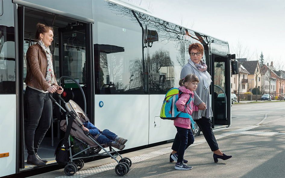 Two women, one with a child in a buggy, and one child leaving a modern city bus