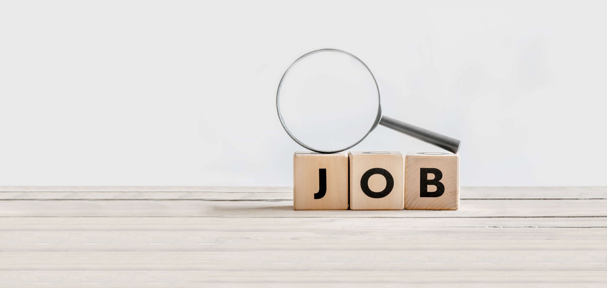 A magnifying glass lying on three letter blocks spelling the word "Job"