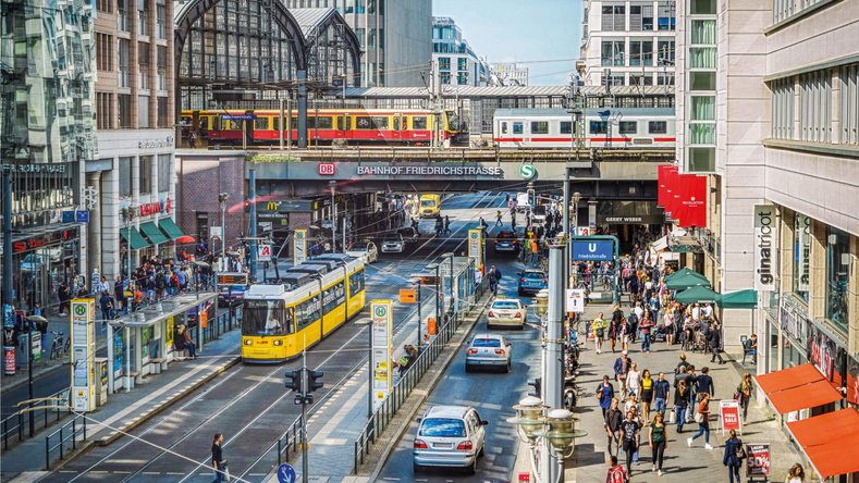 Busy Friedrichstraße in Berlin with S-Bahn, yellow tram, pedestrians and Friedrichstraße station in the background