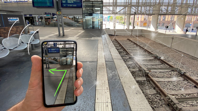 On a railway station, a hand holds a smartphone that indicates a path on the track by arrow.