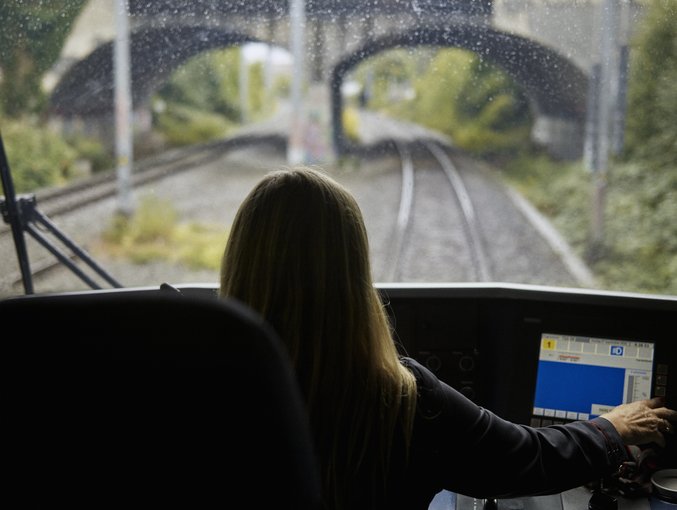 Frau im Führerstand blickt auf Gleise durch Frontscheibe mit Laptop im Vordergrund