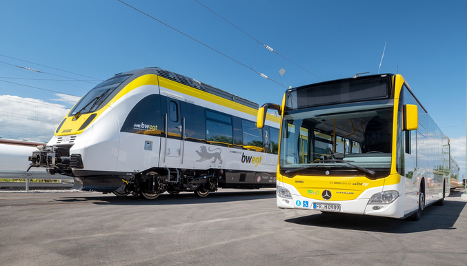 An empty yellow and white bus and a yellow and white SWEG train stand next to each other in a depot.