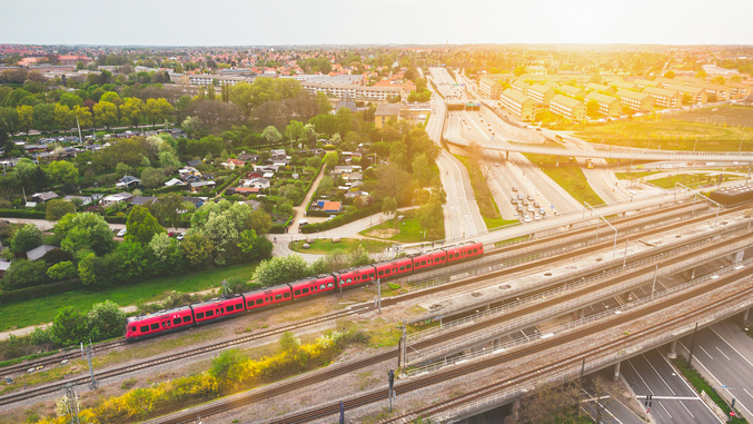 Aerial of a red DSB commuter train travelling through Copenhagen against the setting sun.