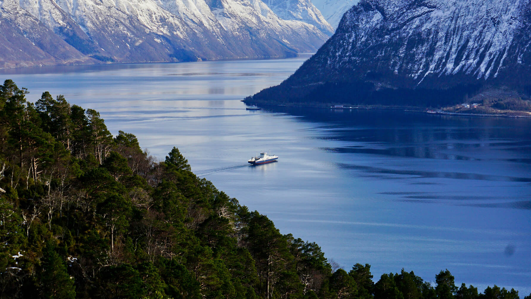 Ferry on river between snow mountains and forest in Norway