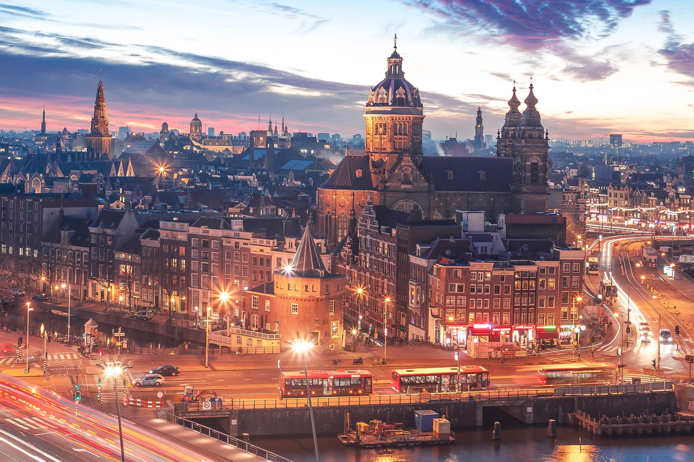 Panorama de Ámsterdam al atardecer con iglesias históricas y estelas de luz del tráfico
