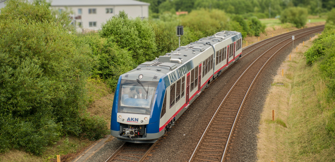 A blue-white-red AKN train runs near a small town in the countryside.