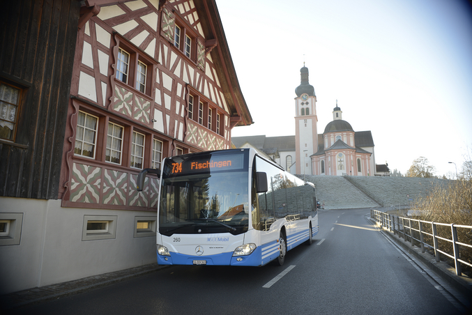 A blue and white bus in front of a monastery in the city centre.