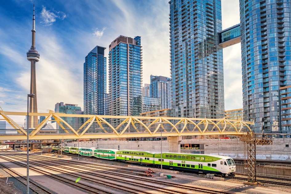 Green and white regional train from GO Transit in front of high-rise buildings in Toronto