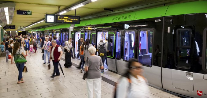 Fahrgäste steigen an belebtem U-Bahnhof in grüne U-Bahn-Züge ein und aus