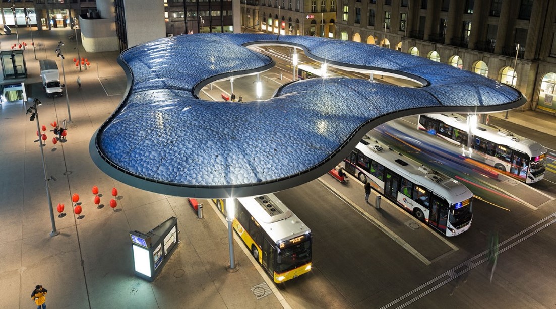 Aarau bus station at night with distinctive blue glass roof structure and buses arriving and departing