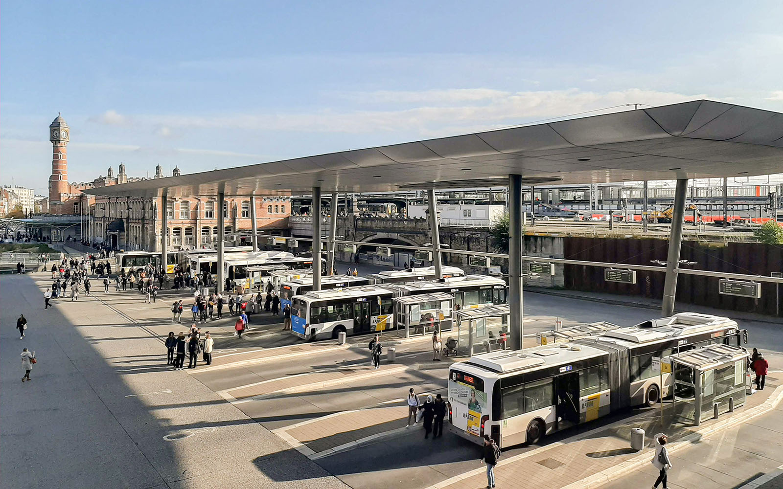 Multiple city buses and passengers at central bus station with covered platforms
