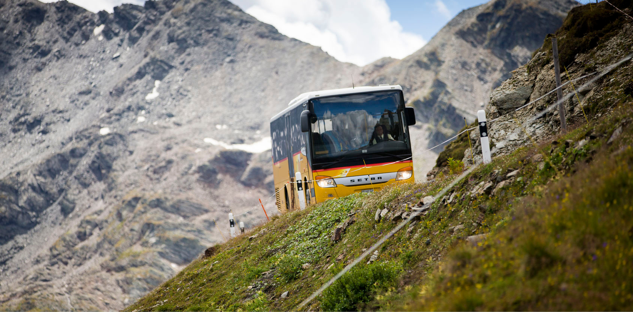 Yellow PostAuto bus travelling on a mountain road in the Alps
