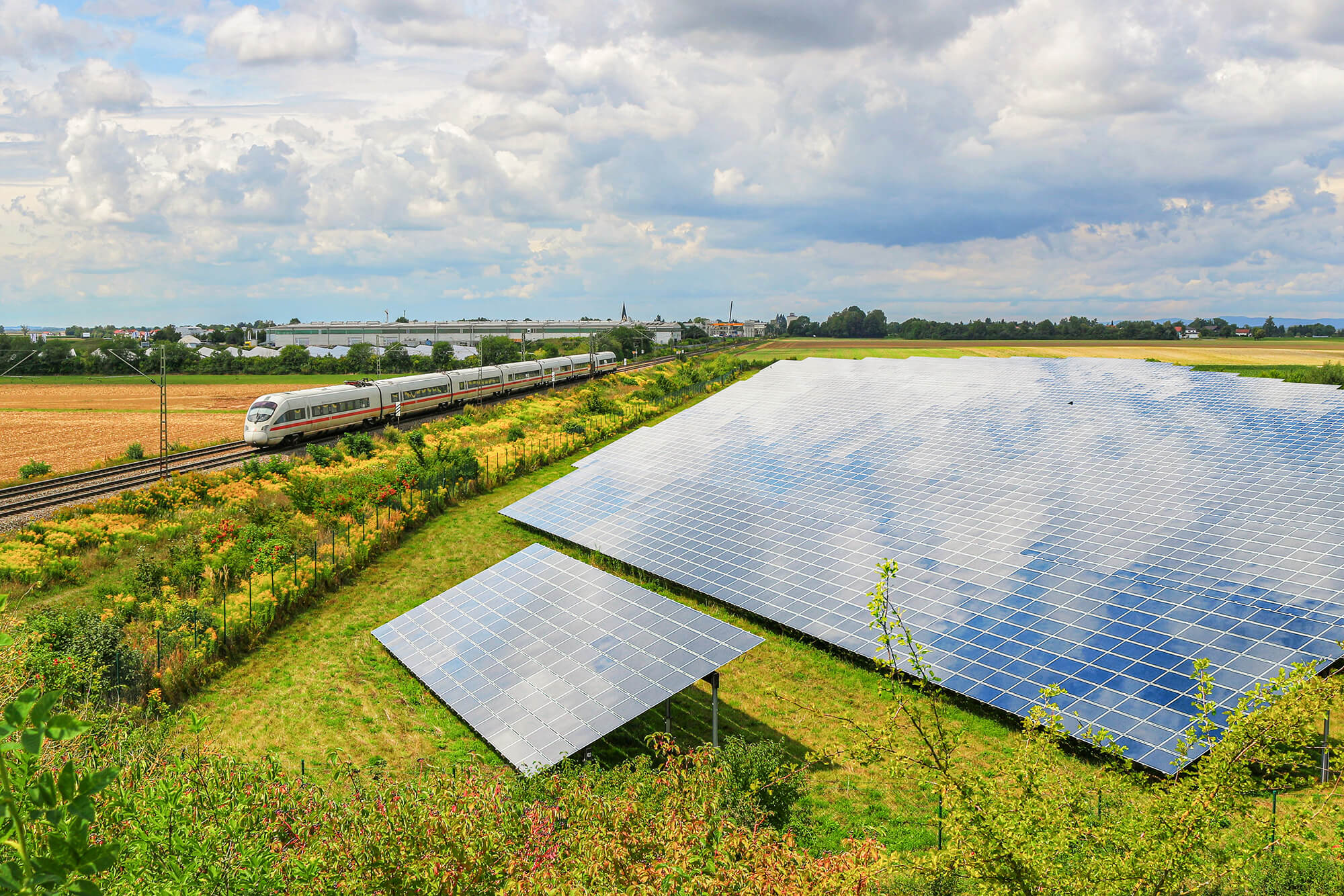 Solar farm on green meadow with train in the background – renewable energy in rail transport