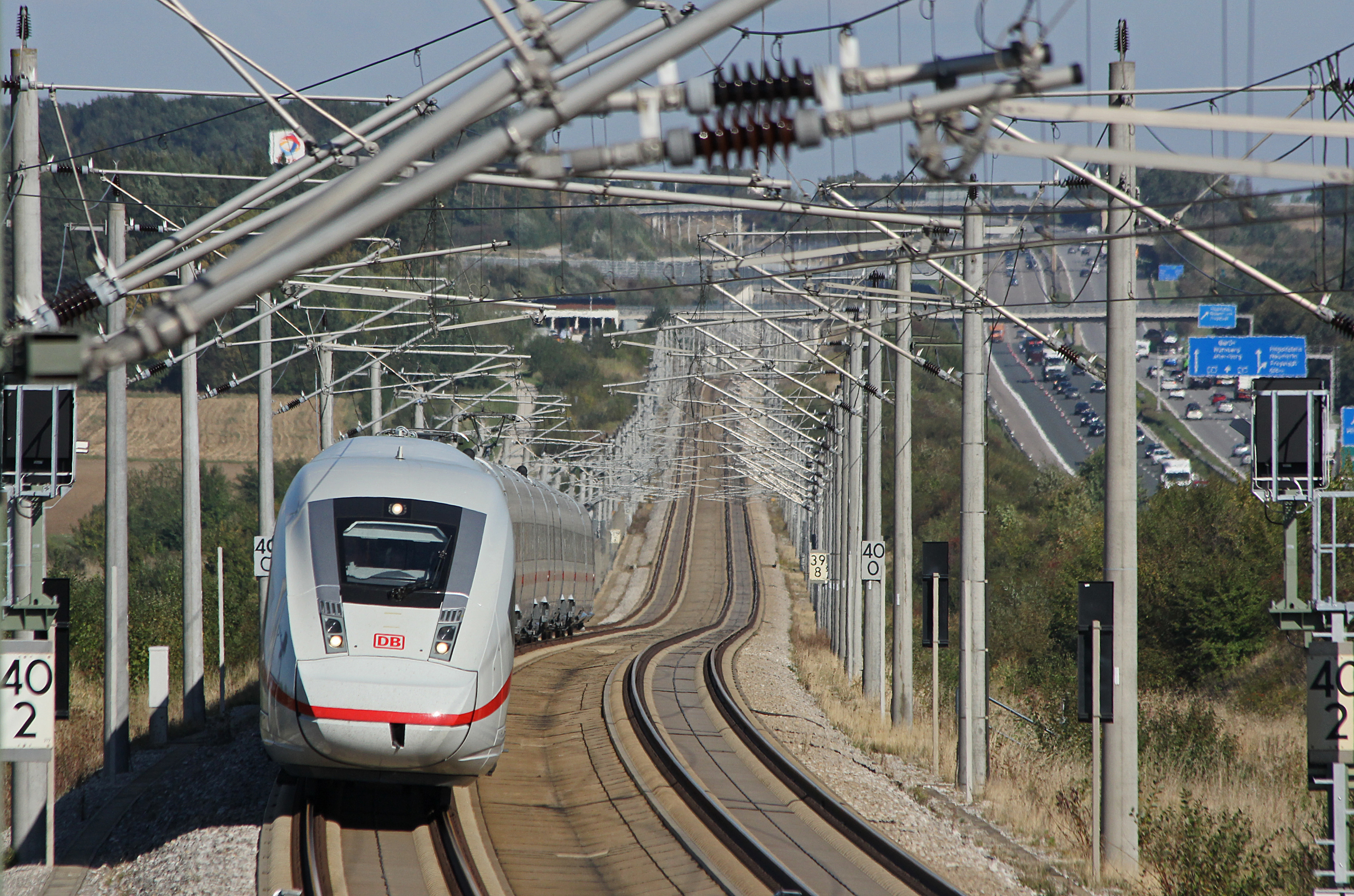 DB Fernverkehr ICE high-speed train in white and red livery running on dual-track line with overhead wires.