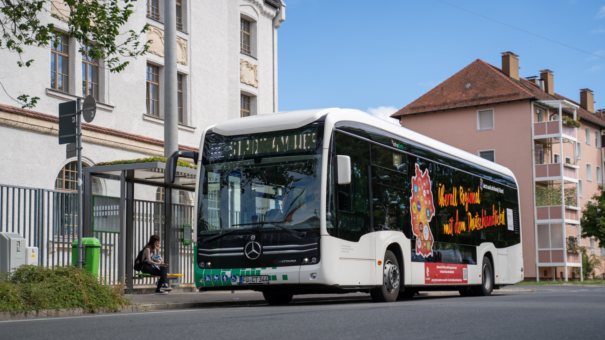 Autobús eléctrico blanco de Infra Fürth con rotulación publicitaria en una parada de autobús en entorno urbano