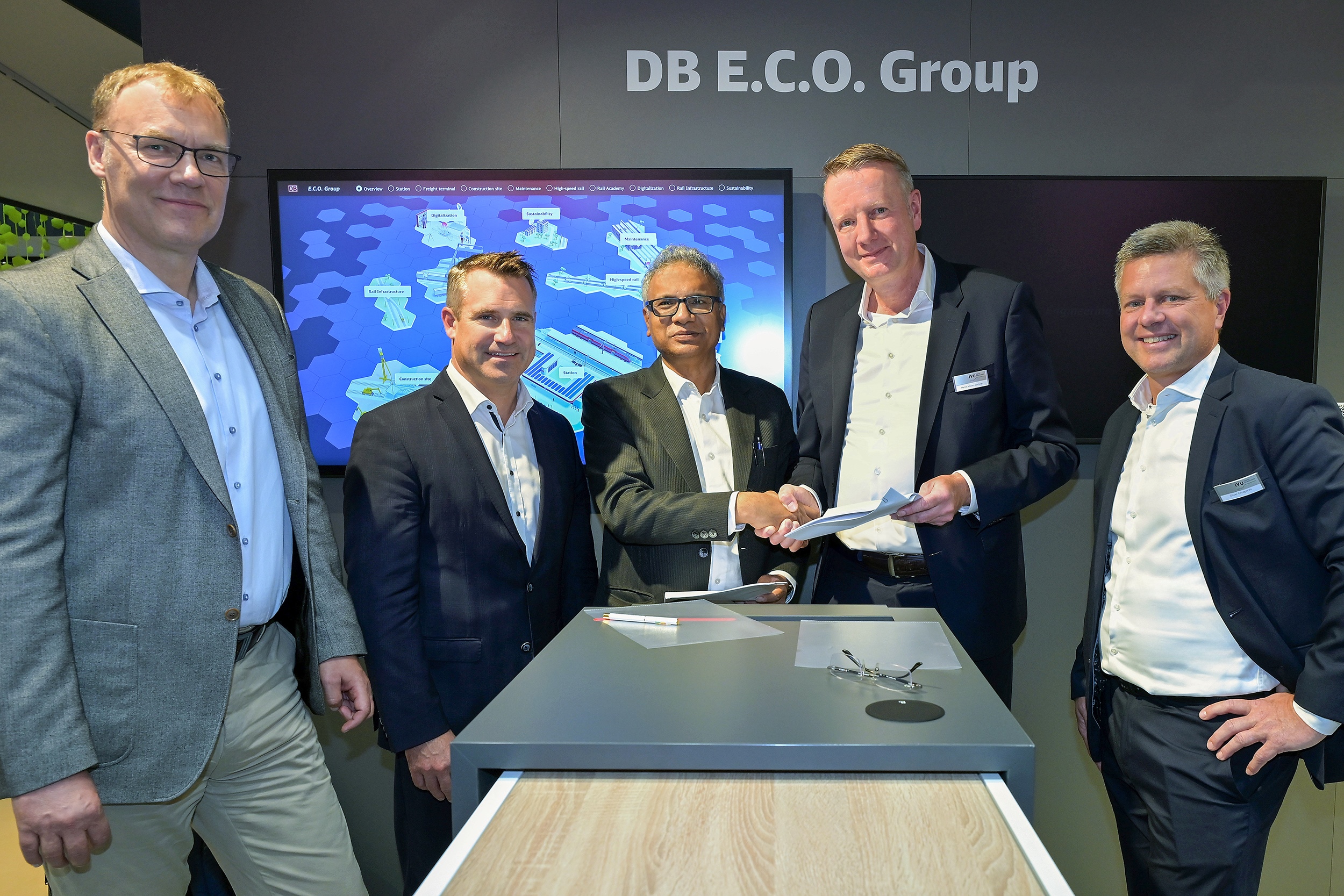 Cinco personas en una firma de contrato frente al banner de DB E.C.O. Group