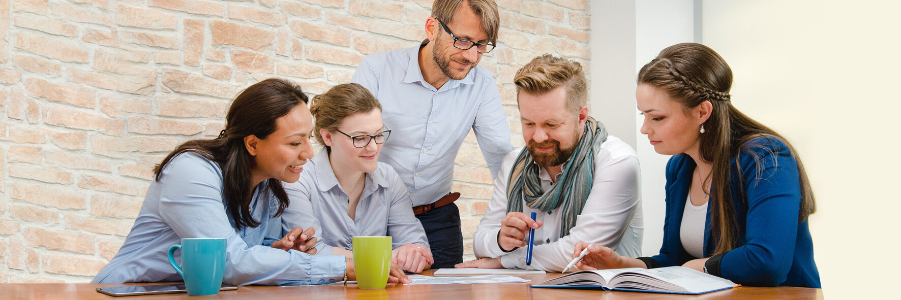 Fünf Kollegen sitzen an einem Tisch und diskutieren die darauf liegenden Dokumente