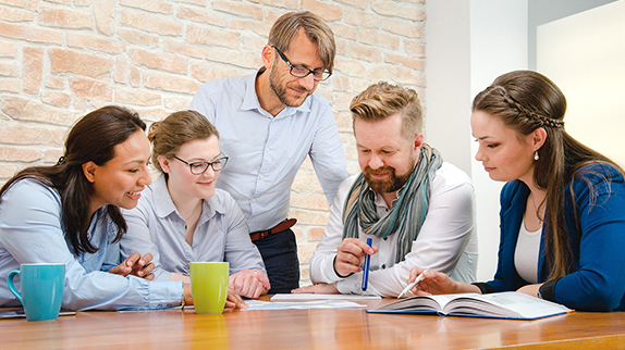 Five colleagues sit at a table and discuss the documents lying on it
